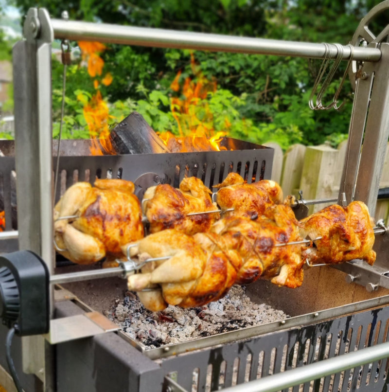 Rotisserie chicken cooking over an open flame outdoors on the Ember Legacy Argentinian grill