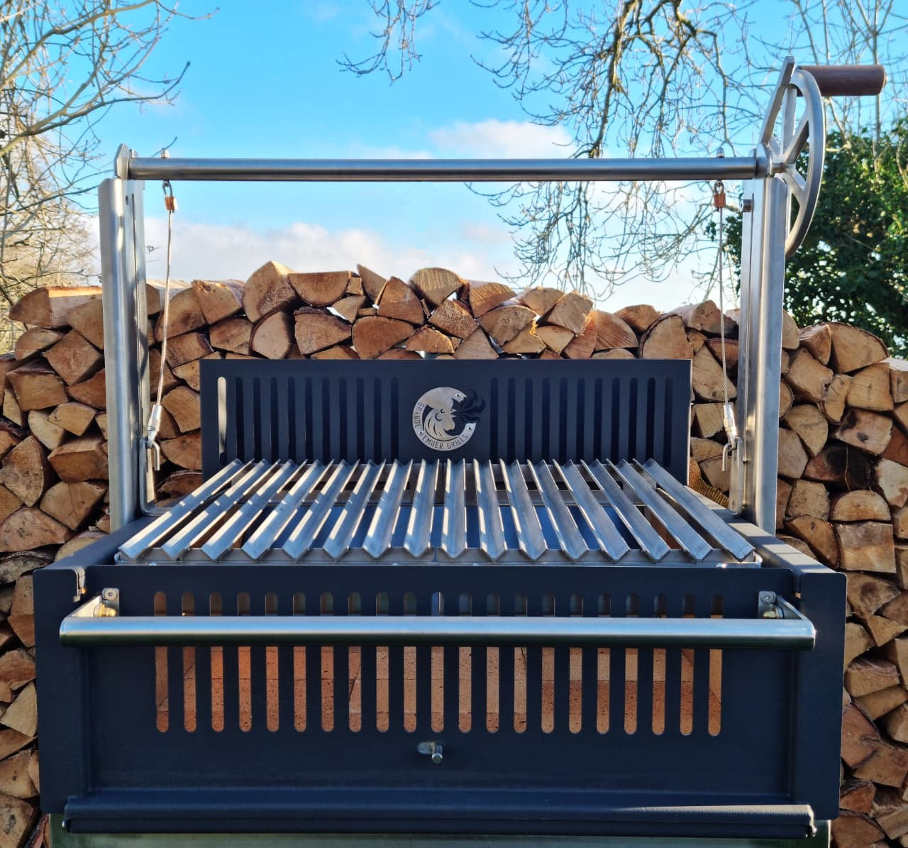 Argentinian barbecue grill with a walnut handle against a backdrop of stacked firewood.