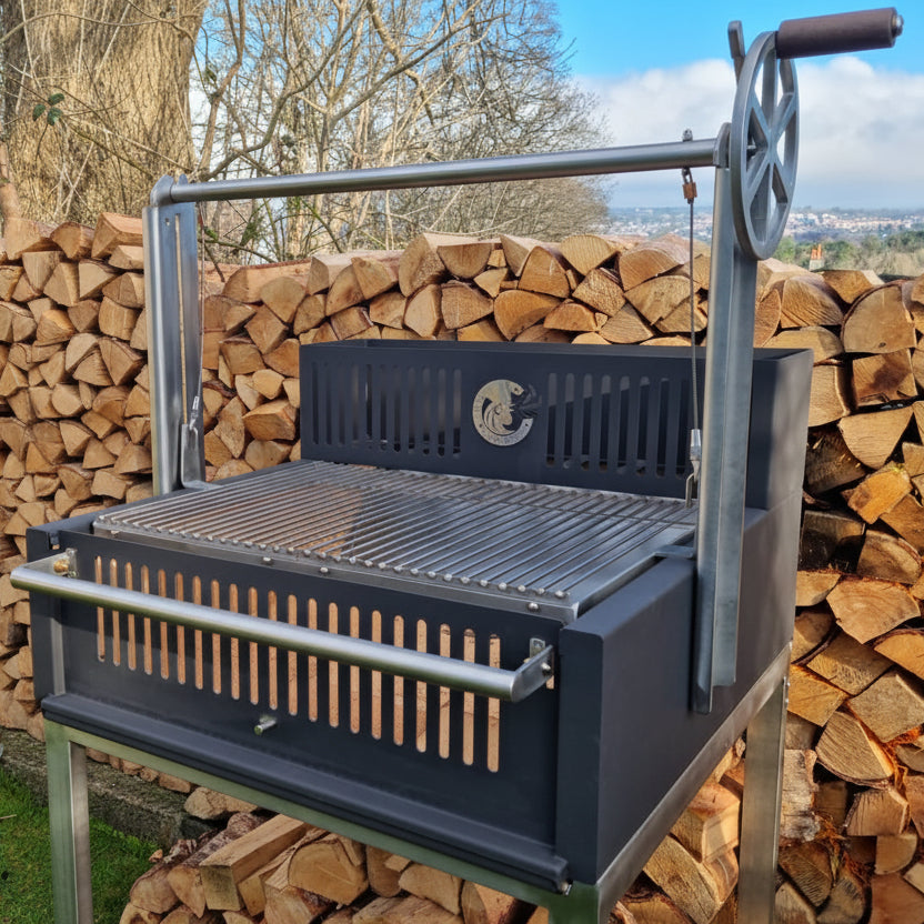 Black Argentinian barbecue grill with metal stand against a background of stacked firewood.