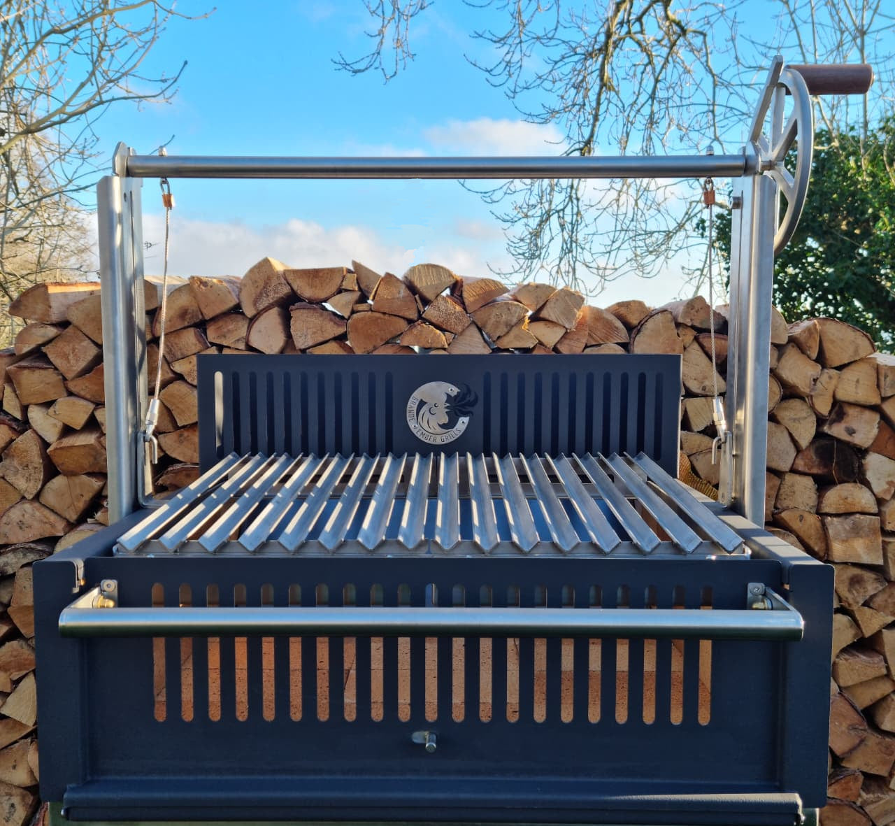 Argentinian grill with logs backdrop with the logo Grande Ember Grills