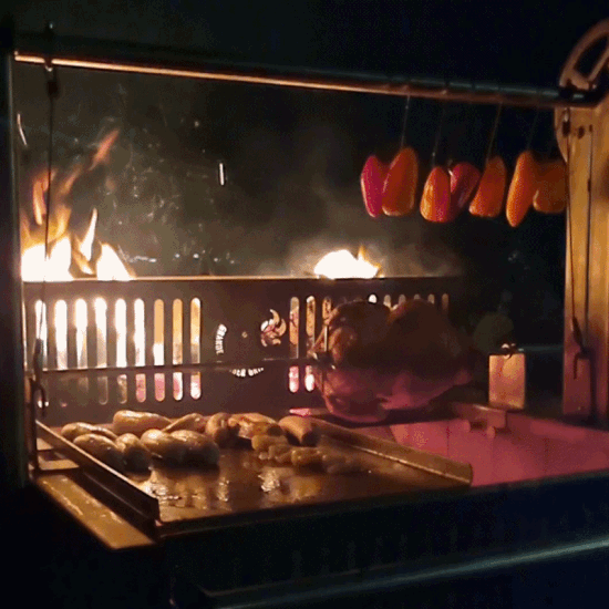 An open fire cookout on the Ember Legacy Argentinian-style BBQ with a juicy slow turning rotisserie chicken and a plancha filled  with shrimp and sausage