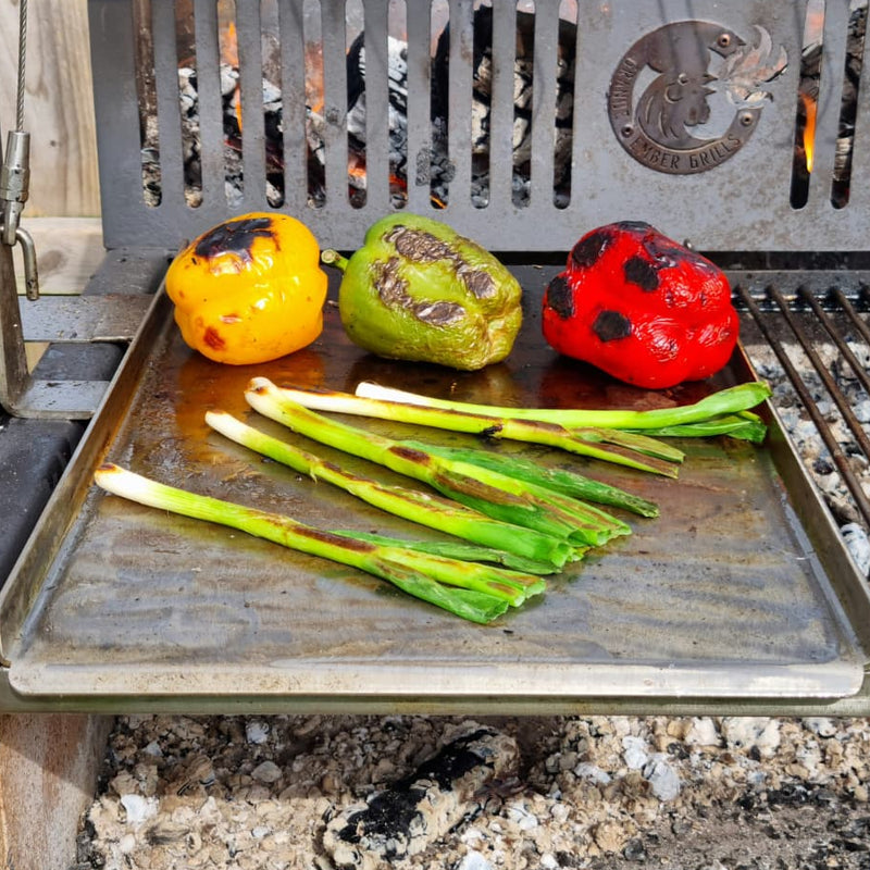 Grilled vegetables including bell peppers and green onions on a stainless steel plancha.